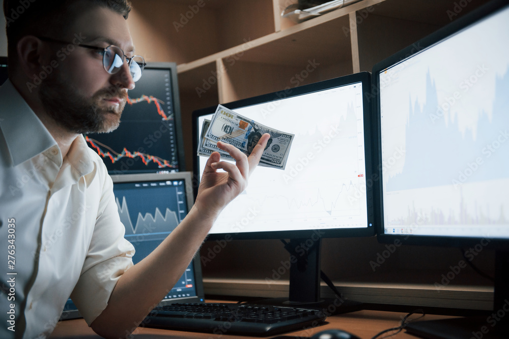 Poster it will cost that much. bearded man in white shirt and glasses holds money in the office with multip