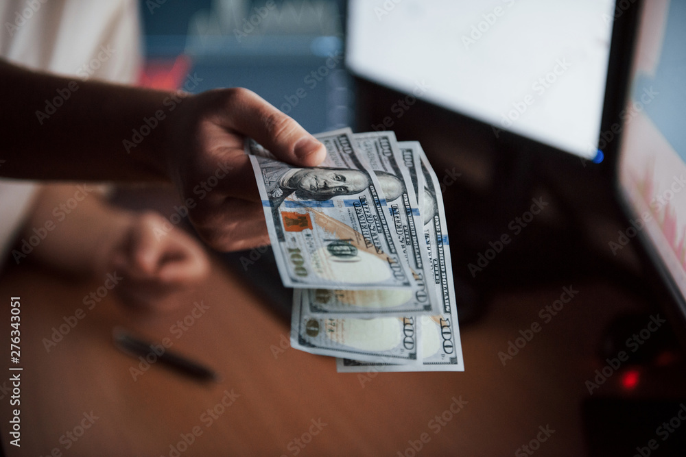 Poster it's your payment. bearded man in white shirt holds money in the office with multiple computer scree