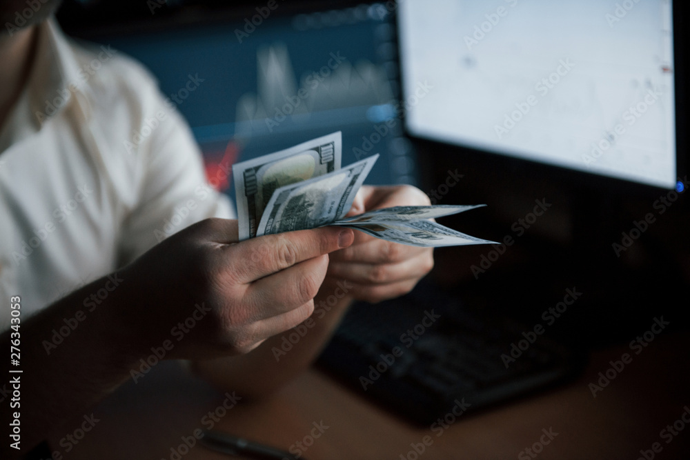 Poster checking his payment. bearded man in white shirt counts money in the office with multiple computer s