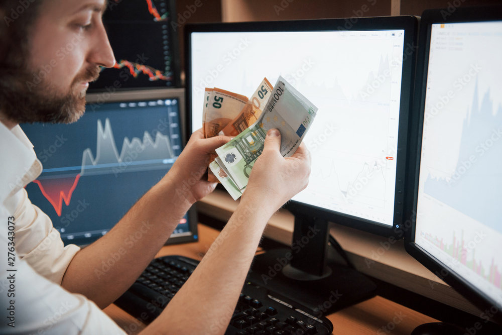 Poster time to get paid. bearded man in white shirt holds earned money in the office with multiple computer