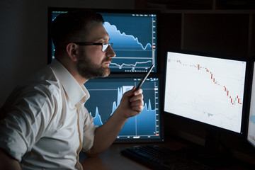 Exchange conception. Bearded man in white shirt works in the office with multiple computer screens in index charts