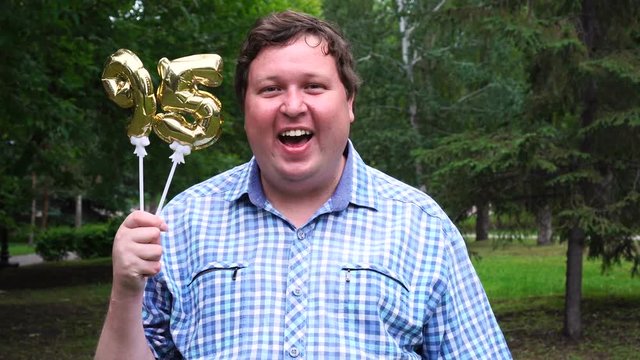 Big man holding golden balloons making the 95 number outdoor. 95th anniversary celebration party