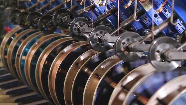 Steel wire coils at a tire factory. Rotating and reeling metal threads bobbins long line at modern tire production plant. Bronze wire is fed for the manufacture of the side rings of automotive wheels.