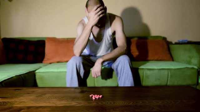 Depressed man suffering from suicidal depression want to commit suicide by overdose taking strong medicament drugs and pills pain killers sitting in his dark room selective focus moody dramatic look