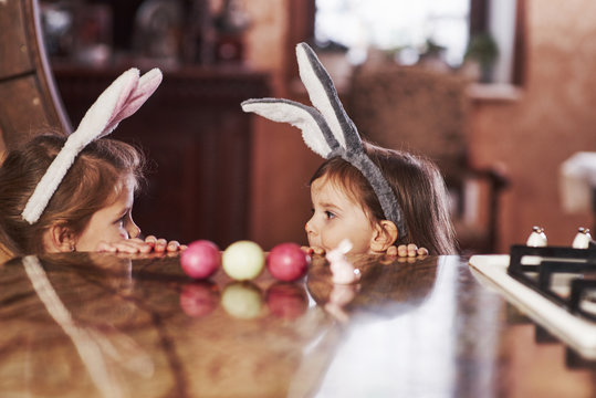 Looks at each other. Funny two sisters in bunny ears looking at each other on the table
