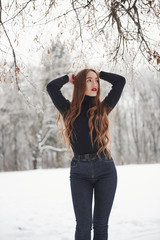 Vertical photo. Pretty girl with long hair and in black blouse is in the winter forest