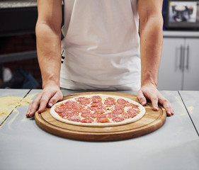 Close up view of baker with pizza that ready to put in the oven to cook