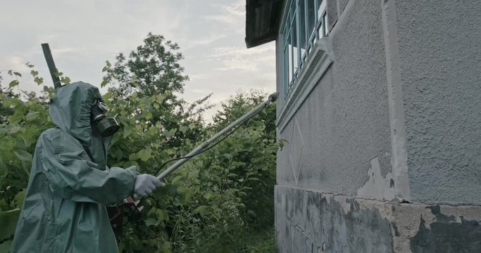 Man in the WWII Hazmat suit and gas mask checking the exterior of an old dilapidated building with a probe for hazardous chemical contamination and radiation. RAW video record.