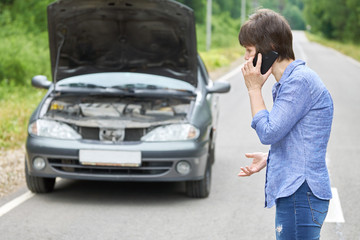 Worried woman talks on the phone near her old broken car on the road