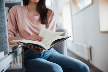 Close up view. Brunette girl in casual clothes having good time in the library full of books