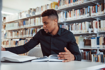 Having research. African american man sitting in the library and searching for some information in the books