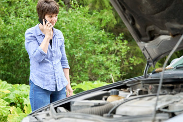 Worried woman talks on the phone near her old broken car