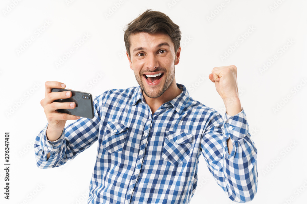 Poster photo of delighted man in casual shirt playing video game on cellphone and clenching fist