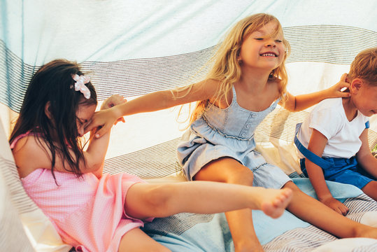 Horizontal image of happy children sitting on the blanket, playing together. Cute little girls and little boy smiling broadly and having fun in the park. Cheerful kids playing outdoors