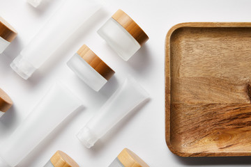 top view of cream tubes and jars near wooden tray on white
