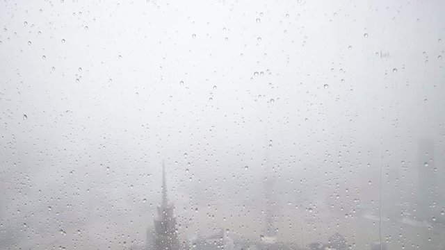 Rain water drops falling on windows glass in summer, super slow motion, heavy rain fall with Shanghai Bund landmarks background.