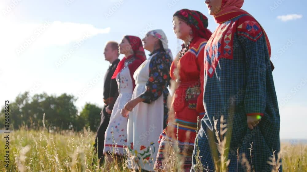 Wall mural Women and man in traditional folk clothes walking in a row on the field and singing a song