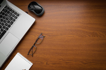 Wood office desk table with laptop, glasses, notebook, pen, smartphone. Top view, copy space