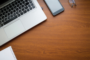 Wood office desk table with laptop, glasses, notebook, pen, smartphone. Top view, copy space