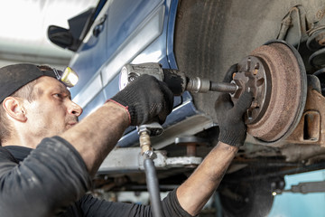 Car mechanic repairs the rear brake drum, unscrews with a pneumatic gun