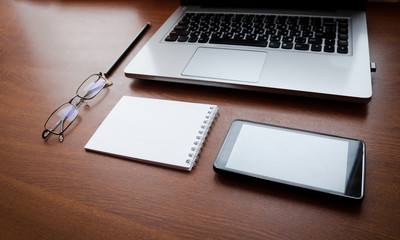 Wood office desk table with laptop, glasses, notebook, pen, smartphone. Top view, copy space