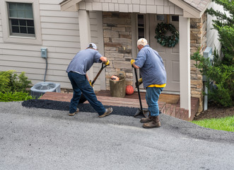 Two workers applying a layer of tarmac or extra blacktop onto asphalt street