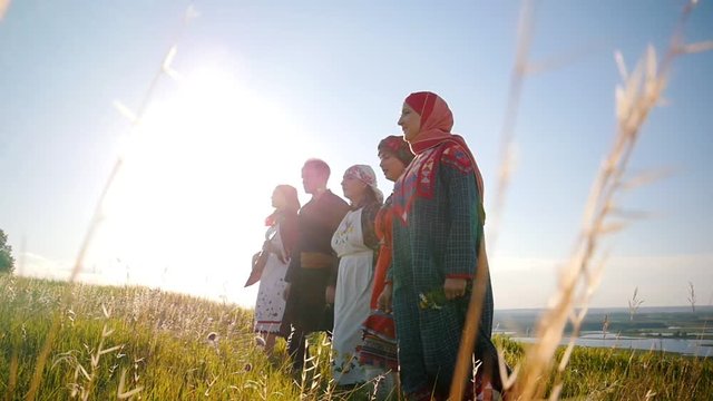 Women and man in traditional russian clothes walking in a row on the field and singing a song