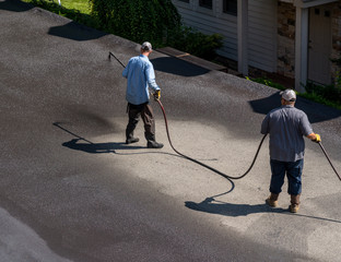 Workers applying blacktop sealer to asphalt street using a spray to provide a protective coat...