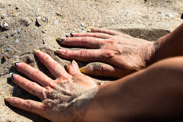 Woman's hands with manicured nails holds hot sand on a beach