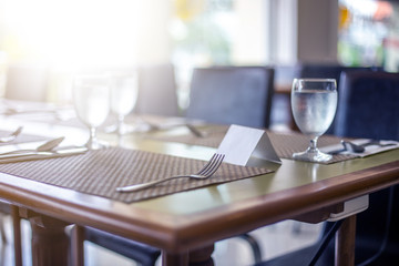 The tables and chairs in the restaurant with full set preparation next to the window with flare in the afternoon , purple shade theme.