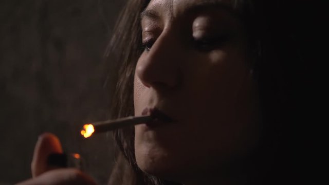 young woman lighting a joint of marijuana in the darkness-slow motion