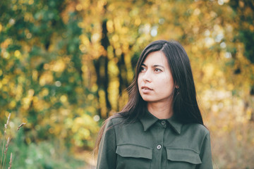 Female beauty portrait surrounded by vivid foliage. Dreamy beautiful girl with long natural black hair on autumn background with colorful leaves in bokeh. Inspired girl enjoys nature in autumn forest.