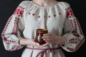 Closeup of part of a woman in Ukrainian embroidered shirt with a pot in her hands on a black background