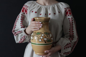 Closeup of part of a woman in Ukrainian embroidery with an earthenware jug in her hands on a black background