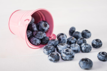 Blueberries in pink bucket on white wooden table.Close up.