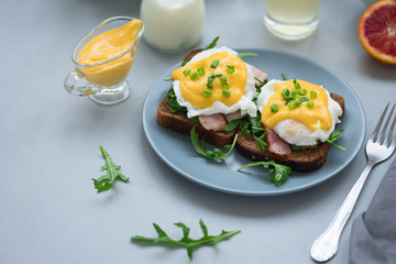 Close up eggs Benedict with arugula, bacon and hollandaise sauce on gray wooden background. Soft focus. Healthy eating concept