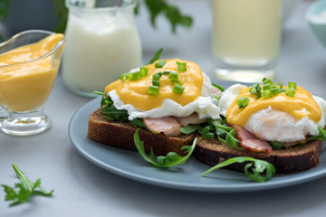 Close up eggs Benedict with arugula, bacon and hollandaise sauce on gray wooden background. Soft focus. Healthy eating concept