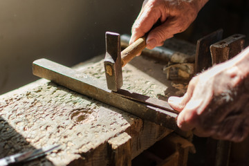 Hands of an elderly man working on the iron with the hammer.