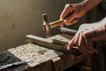 Hands of an elderly man working on the iron with the hammer.