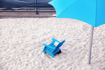 Blue plastic chair and cyan plastic parasol on the white sands of a beach