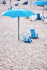 Blue plastic deckchairs and umbrella on the white sands of a beach