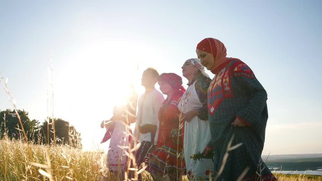 Women and man in traditional russian folklore clothes walking in a row on the field and singing a song - bright sunny summer day