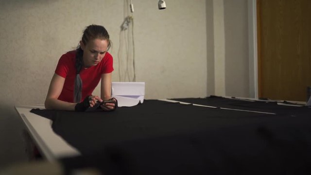 Cyber punk fashion designer at work in her studio cutting pattern - Caucasian white woman wearing red t-shirt and black gloves with scissors hanging over her chest