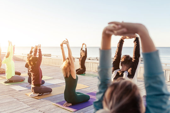 Yoga class at sea beach in evening. Group of people doing yoga poses with calm relax emotion at wooden fitness terrace with young instructor. Meditation pose,Wellness and Healthy balance lifestyle.