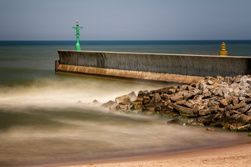 Stormy sea harbour on a sunny day with a beacon, pier and rocks - 276361022