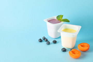 Plastic cups with yogurt and fruits on color background, space for text