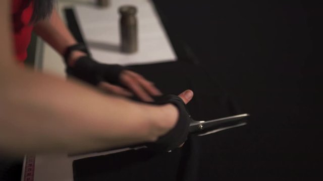 Cyber punk fashion designer at work in her studio cutting pattern - Caucasian white woman wearing red t-shirt and black gloves with scissors hanging over her chest