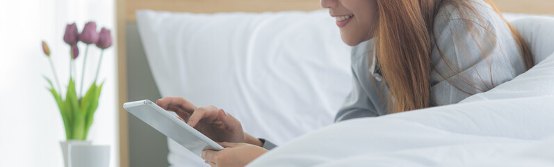 Cropped image of young happy Asian woman lie down on bed and playing smart tablet in modern bedroom © Supagrit Ninkaesorn