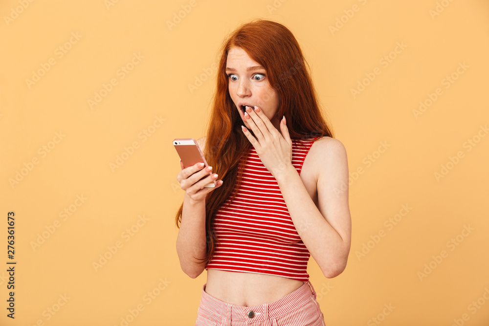 Canvas Prints Shocked emotional cute young pretty redhead woman posing isolated over yellow background using mobile phone chatting.