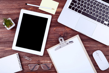 Laptop and tablet computer with glasses, clipboard, mouse on wooden table